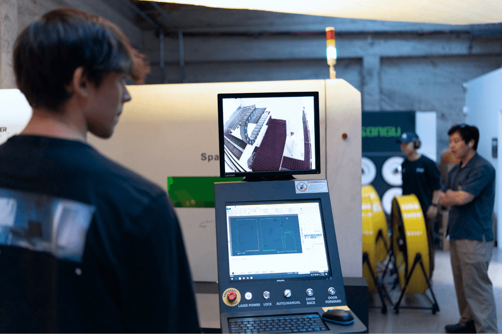 Zain beside a laser cutter in the factory